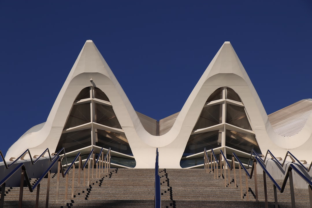 Symmetrical view up the stairway to the Museu de les Ciències at Valencia’s City of Arts and Sciences, sleek white gables cutting into a deep blue sky, railings zig-zagging like a heartbeat toward the glassy apex.